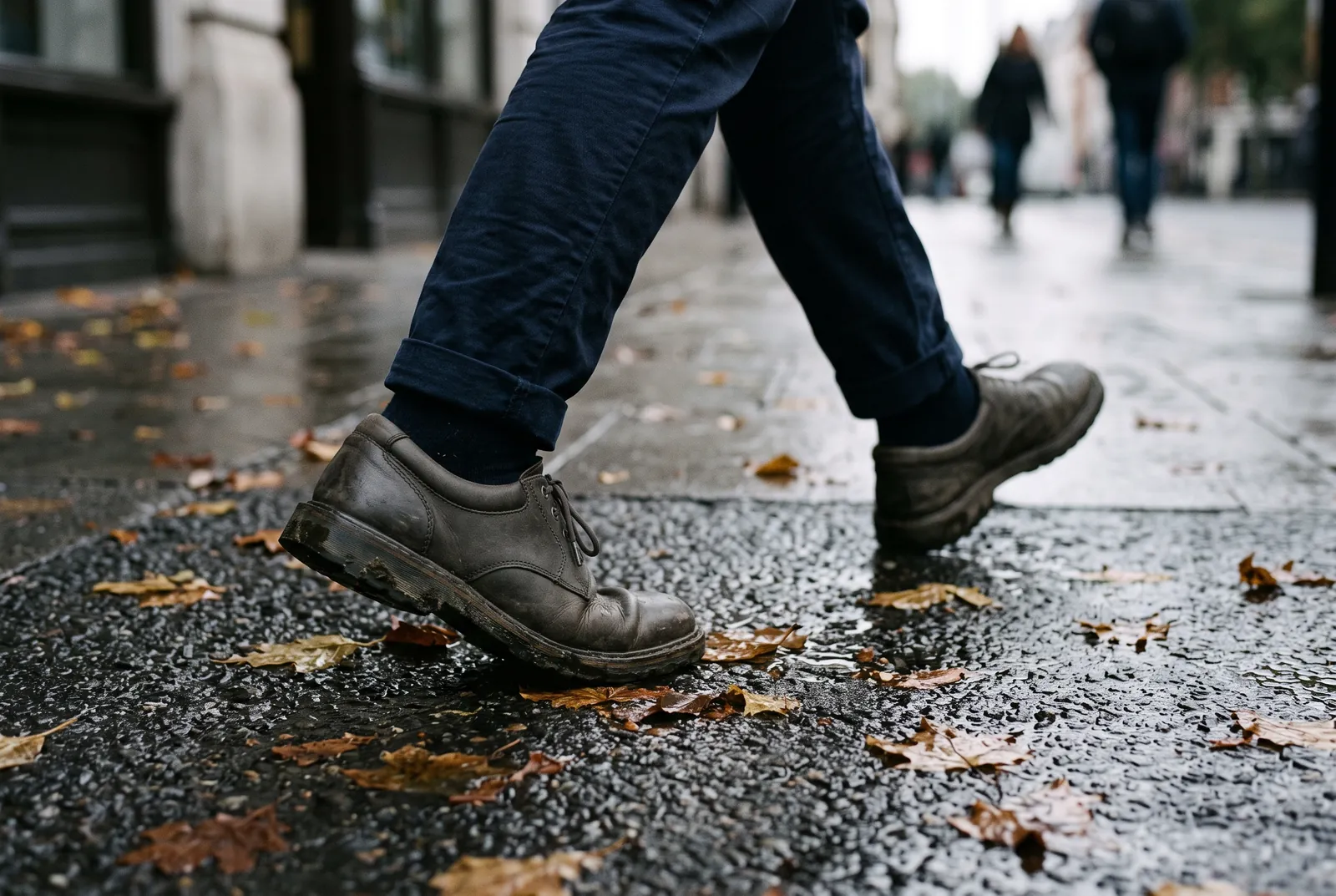 Les jambes d'un passant marchant sur un trottoir humide couvert de feuilles mortes
